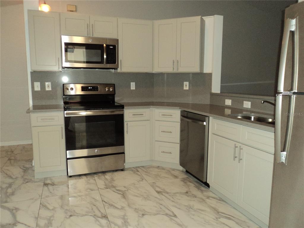 A kitchen features light gray cabinets, stainless steel appliances, and white marble-patterned tile flooring — 548 E MONTROSE STREET, CLERMONT, FL