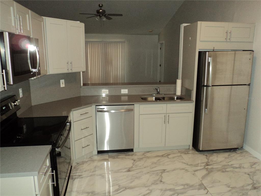 A kitchen features light gray cabinets, stainless steel appliances, and white marble-patterned tile flooring — 548 E MONTROSE STREET, CLERMONT, FL