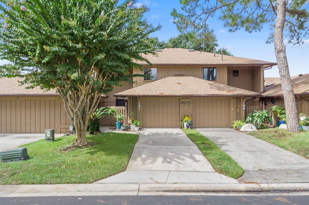 A two-story brown townhouse with two garages, a concrete driveway, and a large tree — 182 HERON BAY CIRCLE, LAKE MARY, FL