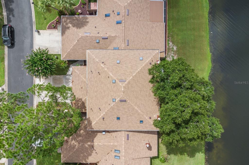 An aerial view shows the shingled roof of a residential building next to a lake — 182 HERON BAY CIRCLE, LAKE MARY, FL