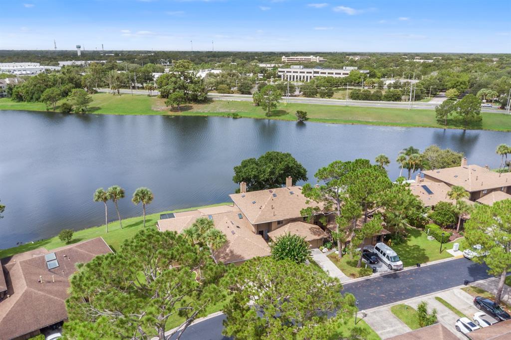 An aerial view shows a multi-unit residential building situated along a lake with surrounding trees — 182 HERON BAY CIRCLE, LAKE MARY, FL