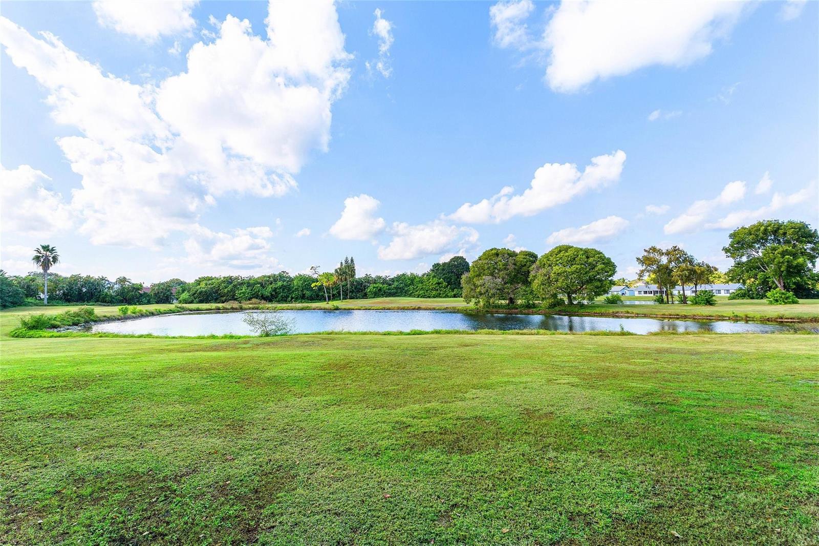 A grassy lawn leads to a pond surrounded by trees under a blue sky — 9286 Vista Del Lago, Boca Raton FL 33428, BOCA RATON, FL