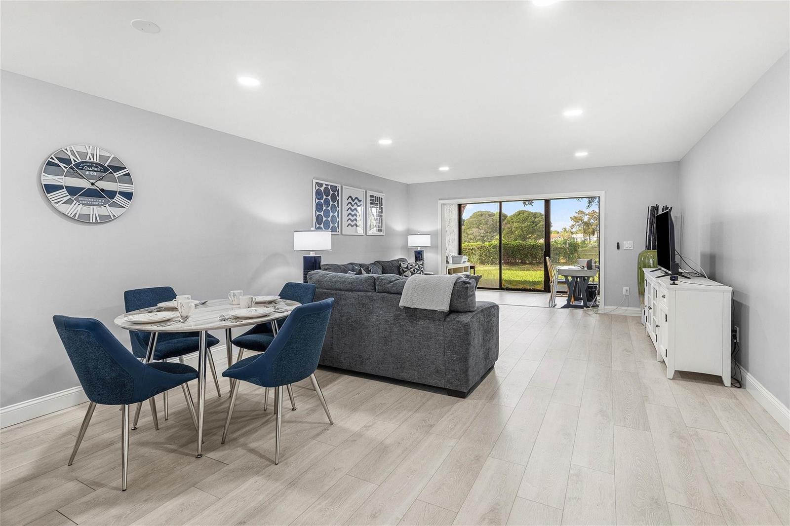 A living and dining area features light wood floors, a grey sofa, and sliding glass doors — 9286 Vista Del Lago, Boca Raton FL 33428, BOCA RATON, FL
