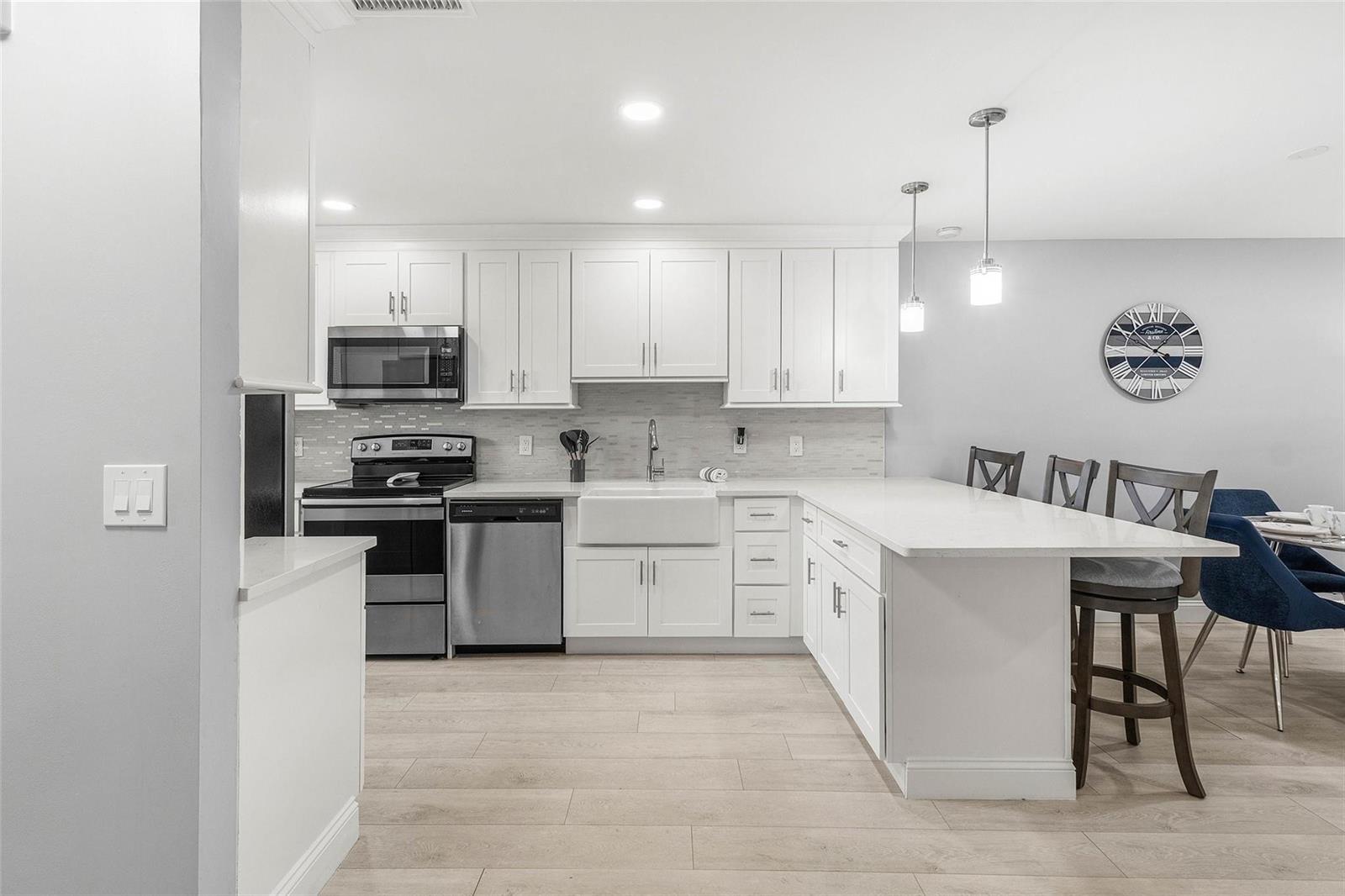 A modern kitchen features white cabinets, stainless steel appliances, a farmhouse sink, and a peninsula — 9286 Vista Del Lago, Boca Raton FL 33428, BOCA RATON, FL
