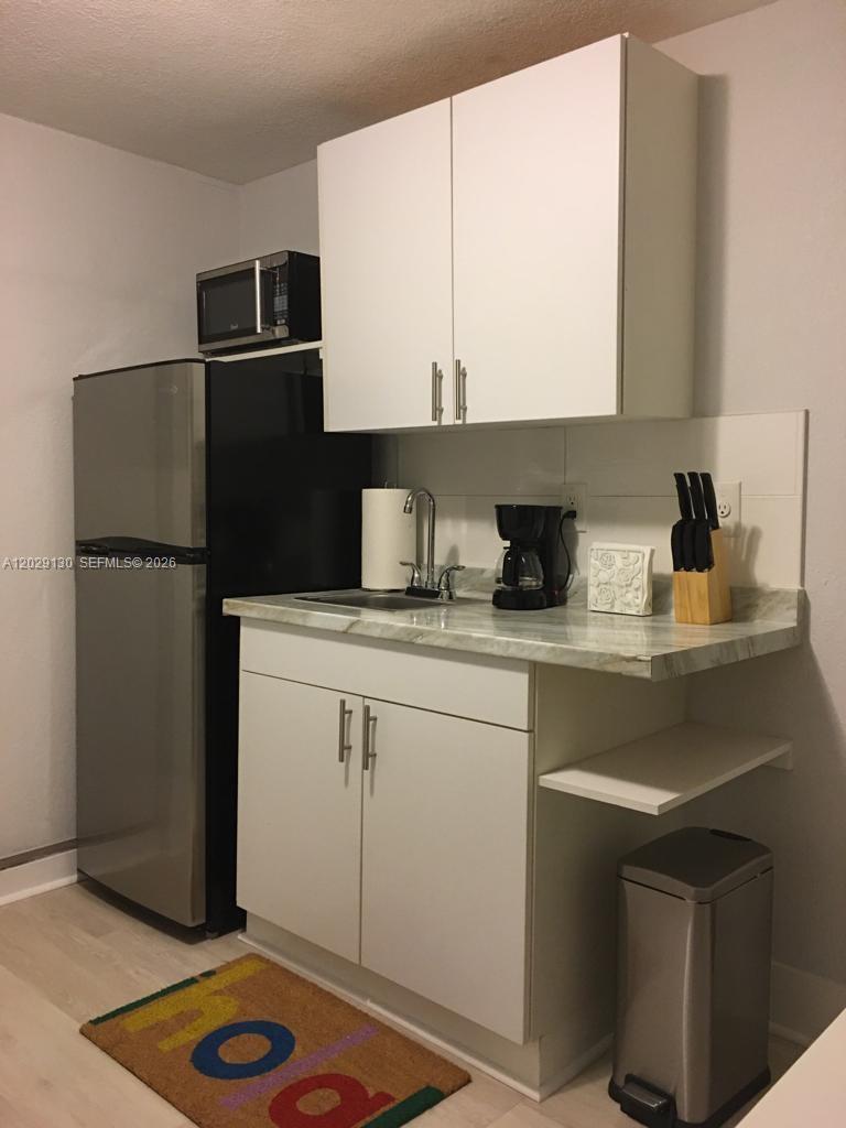 A small kitchen features white cabinets, a stainless steel refrigerator, and a marble-patterned countertop — 7525 S Waterway Dr, Miami FL 33155, MIAMI, FL