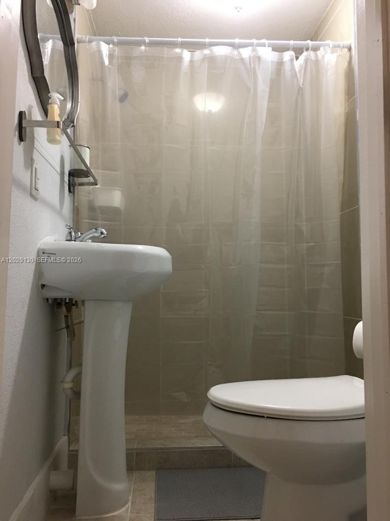 A small bathroom features a pedestal sink, a toilet, and a shower with a curtain — 7525 S Waterway Dr, Miami FL 33155, MIAMI, FL