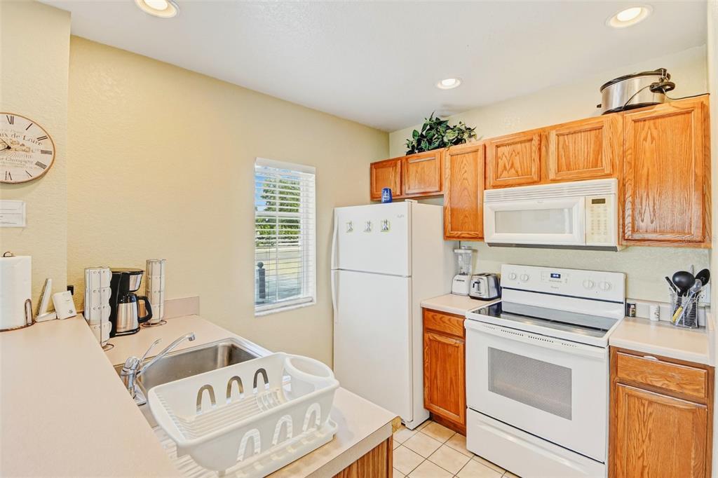 A kitchen features wood cabinets, white appliances, a sink, and a window — 2610 LODI CIRCLE UNIT 107, KISSIMMEE, FL
