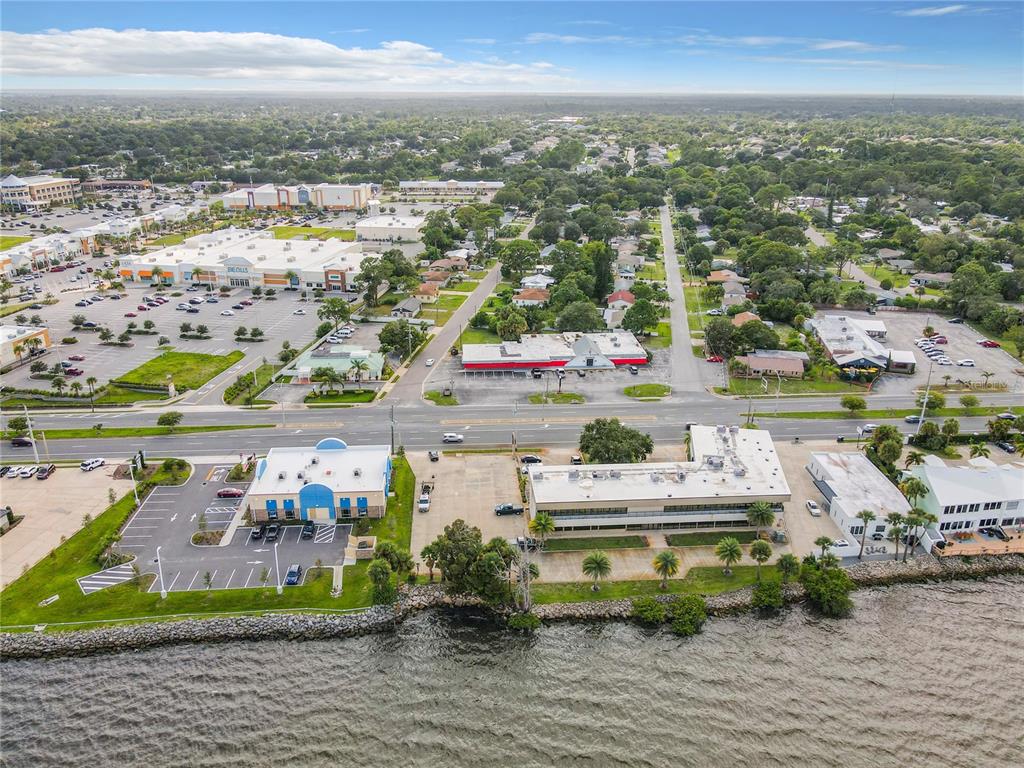 An aerial view shows commercial buildings and a parking lot situated along a waterfront — 2300 S WASHINGTON AVENUE, TITUSVILLE, FL