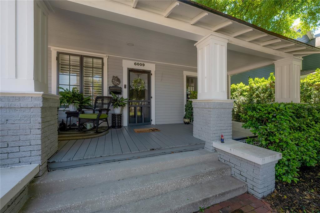 A gray-painted front porch features white columns, a rocking chair, and a screen door — 6009 N SUWANEE AVENUE, TAMPA, FL