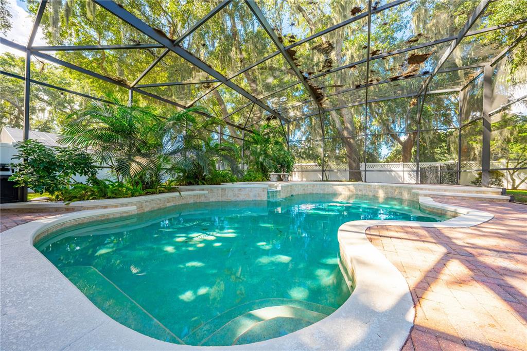 A swimming pool with a stone-tiled spillover feature sits inside a screened-in patio enclosure — 1648 MARINA LAKE DRIVE, KISSIMMEE, FL