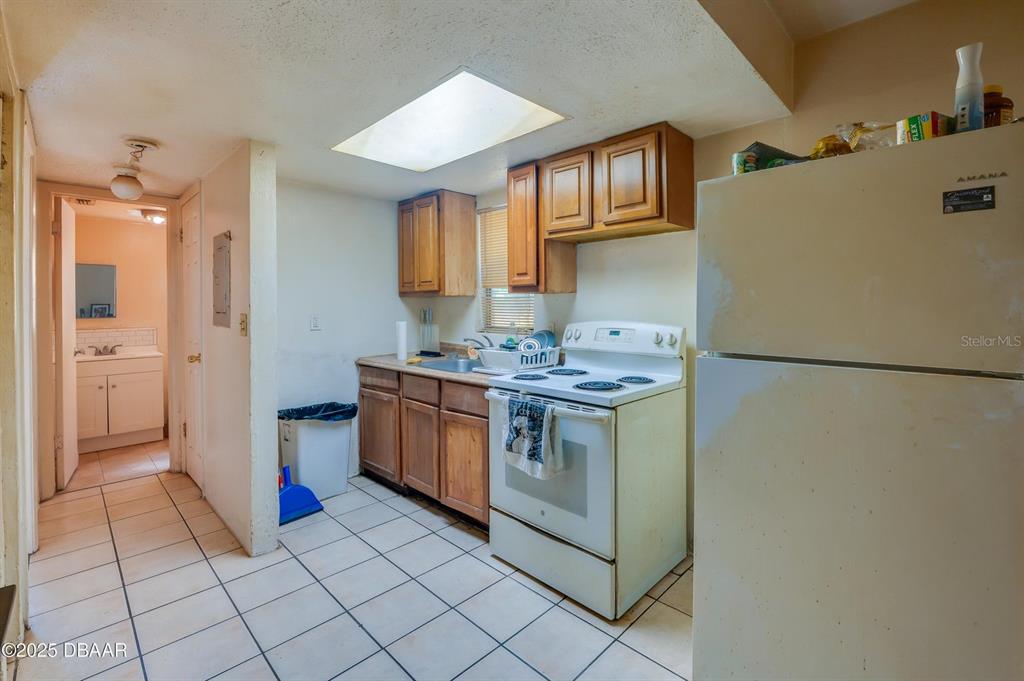 A kitchen features wood cabinets, a white stove, a refrigerator, and tiled flooring — 600 S SEGRAVE STREET, DAYTONA BEACH, FL