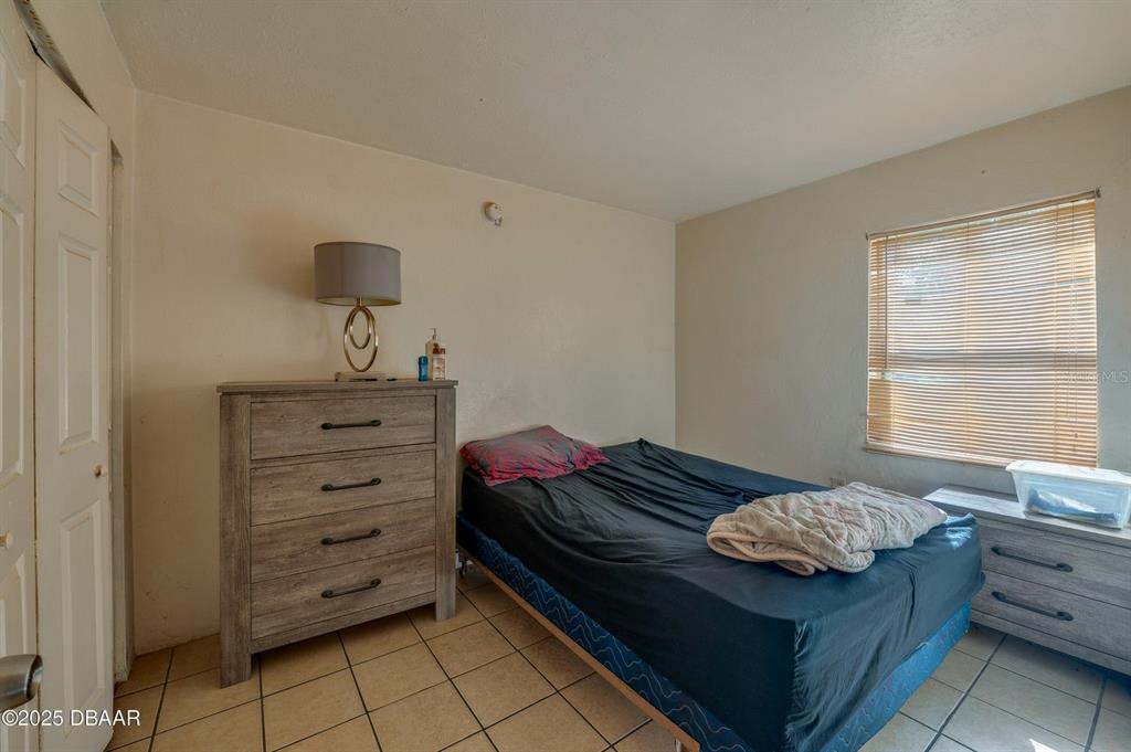 A bedroom features a bed, a wooden dresser, a lamp, and tiled flooring — 600 S SEGRAVE STREET, DAYTONA BEACH, FL