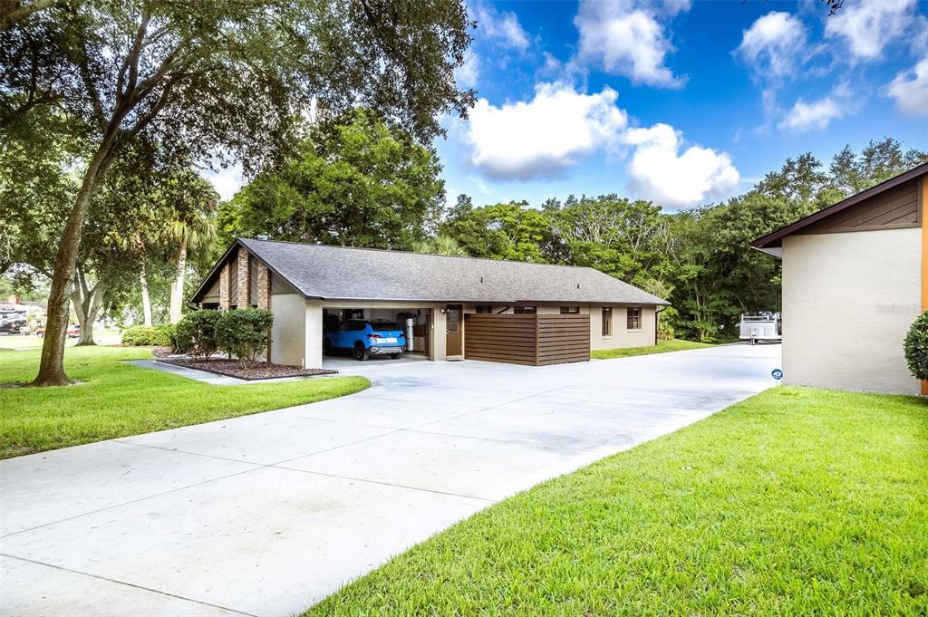 A side view of a house exterior featuring a carport, driveway, and wooden privacy fence — 1930 LONG POND DRIVE, LONGWOOD, FL