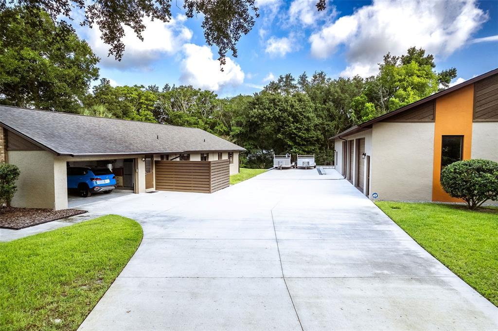 A wide concrete driveway sits between two buildings with a blue car parked under a carport — 1930 LONG POND DRIVE, LONGWOOD, FL