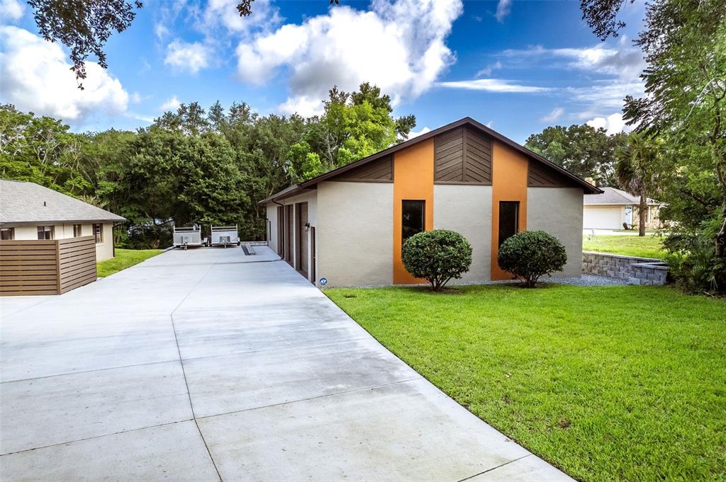 A side view of a house with a large concrete driveway and two small bushes — 1930 LONG POND DRIVE, LONGWOOD, FL