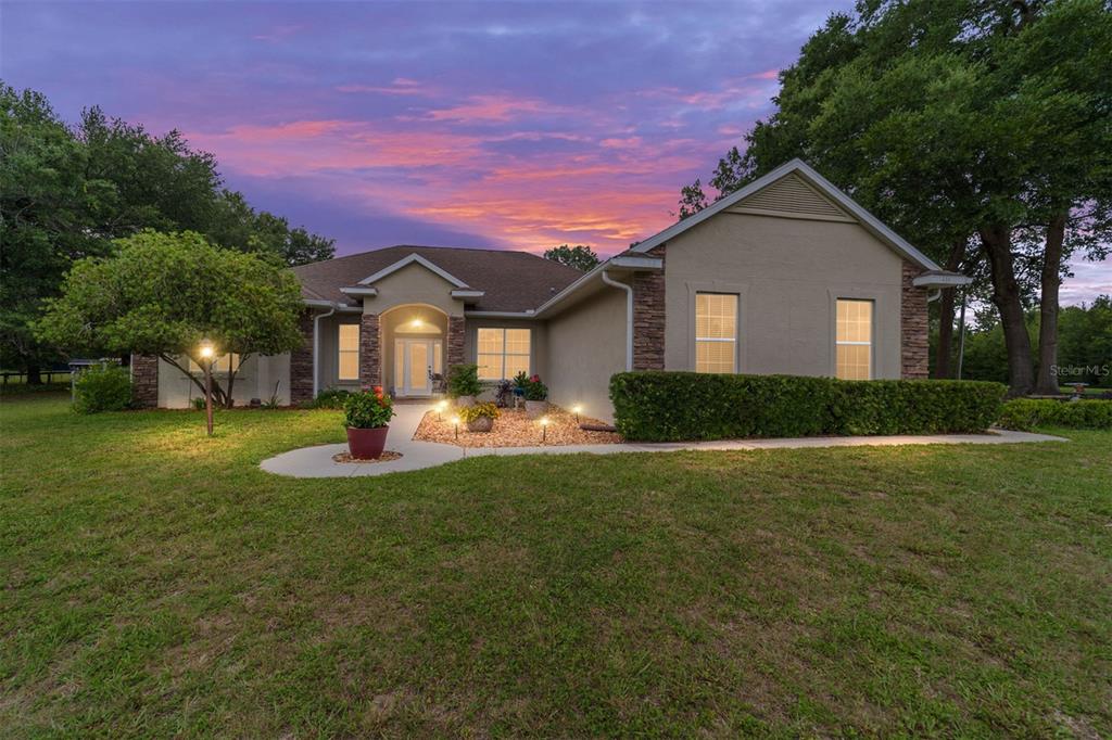 A single-story house with a tan stucco exterior and stone accents at twilight — 435 NE 155TH STREET ROAD, CITRA, FL