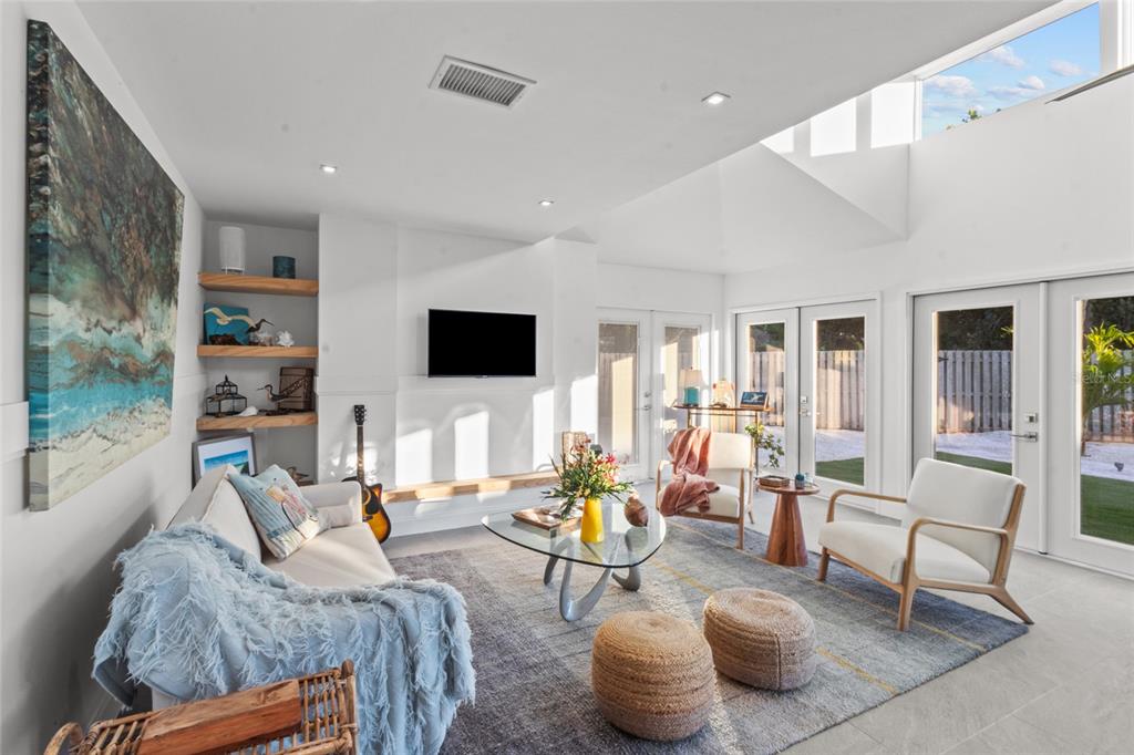 A bright living room features a vaulted ceiling, glass doors, and a modern seating area — 624 SAINT JUDES DRIVE, LONGBOAT KEY, FL