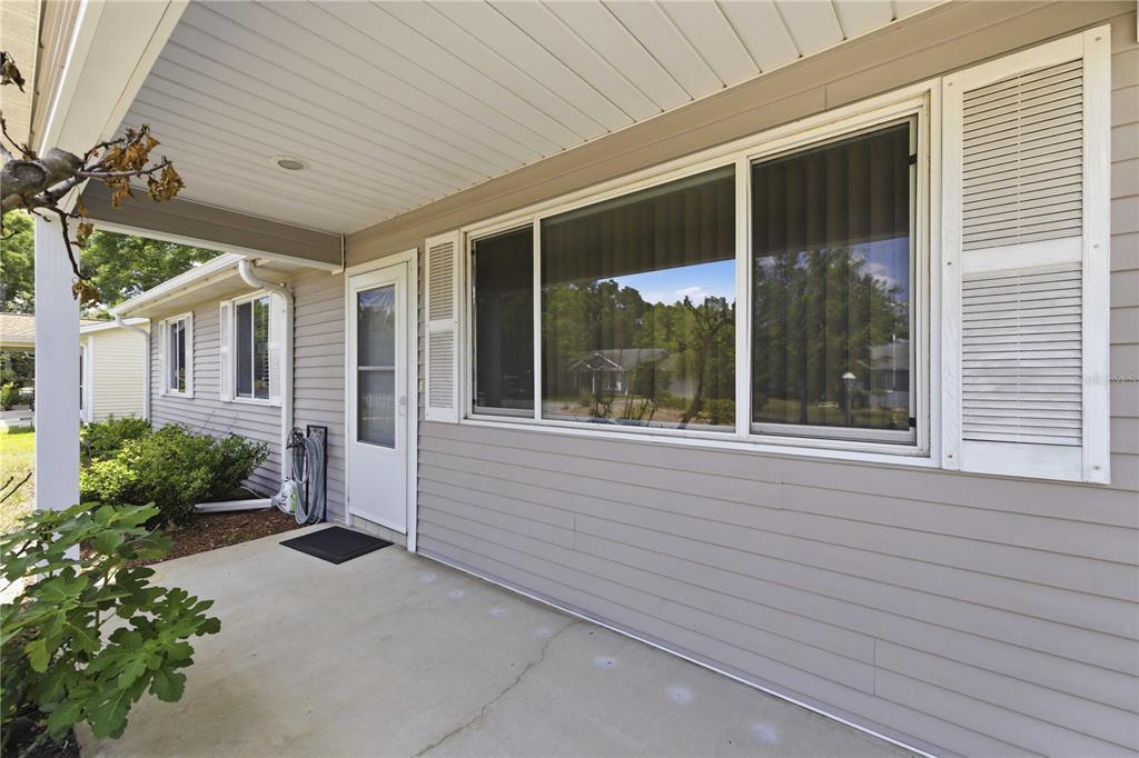 A covered concrete porch features light gray horizontal siding, white shutters, and a glass door — 10986 SW 83RD AVENUE, OCALA, FL
