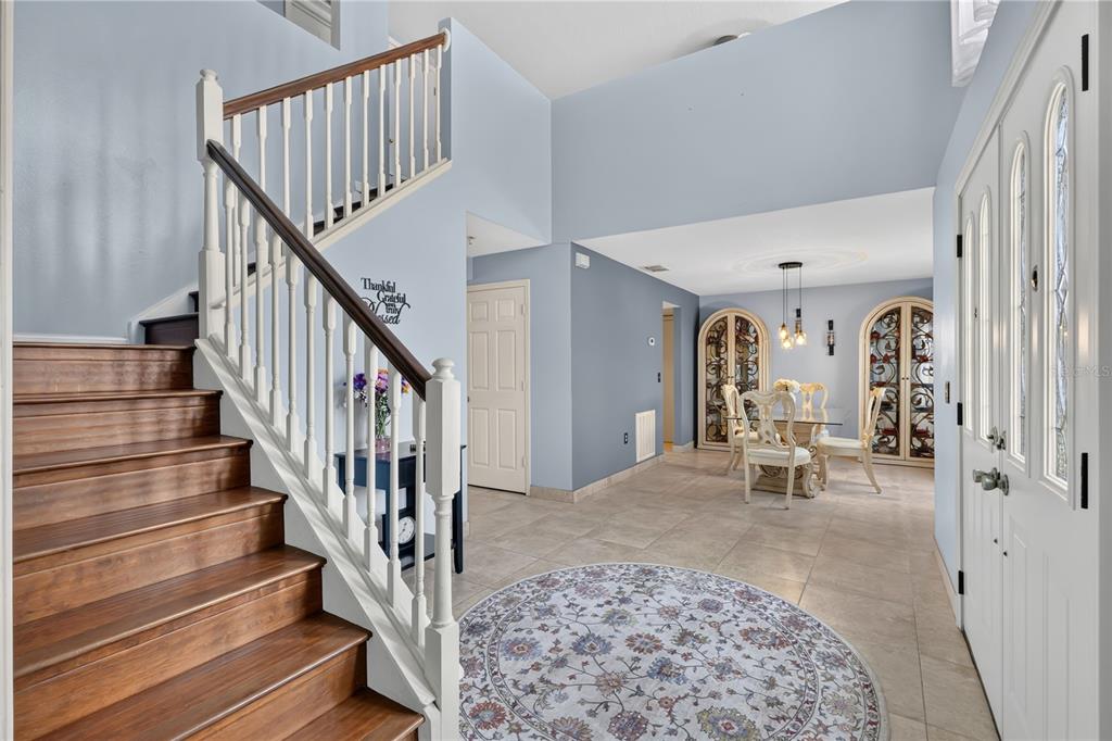 A foyer with a wooden staircase, tile flooring, and a dining area in the background — 4912 NEWTON COURT, ST CLOUD, FL