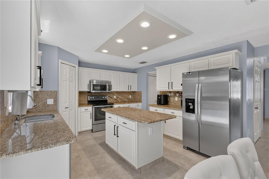 A kitchen features white cabinetry, granite countertops, stainless steel appliances, and a central island — 4912 NEWTON COURT, ST CLOUD, FL
