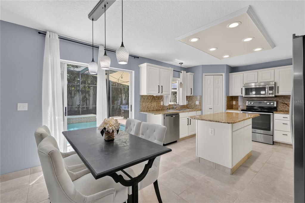 A kitchen with white cabinets, granite countertops, a center island, and an adjacent dining area — 4912 NEWTON COURT, ST CLOUD, FL