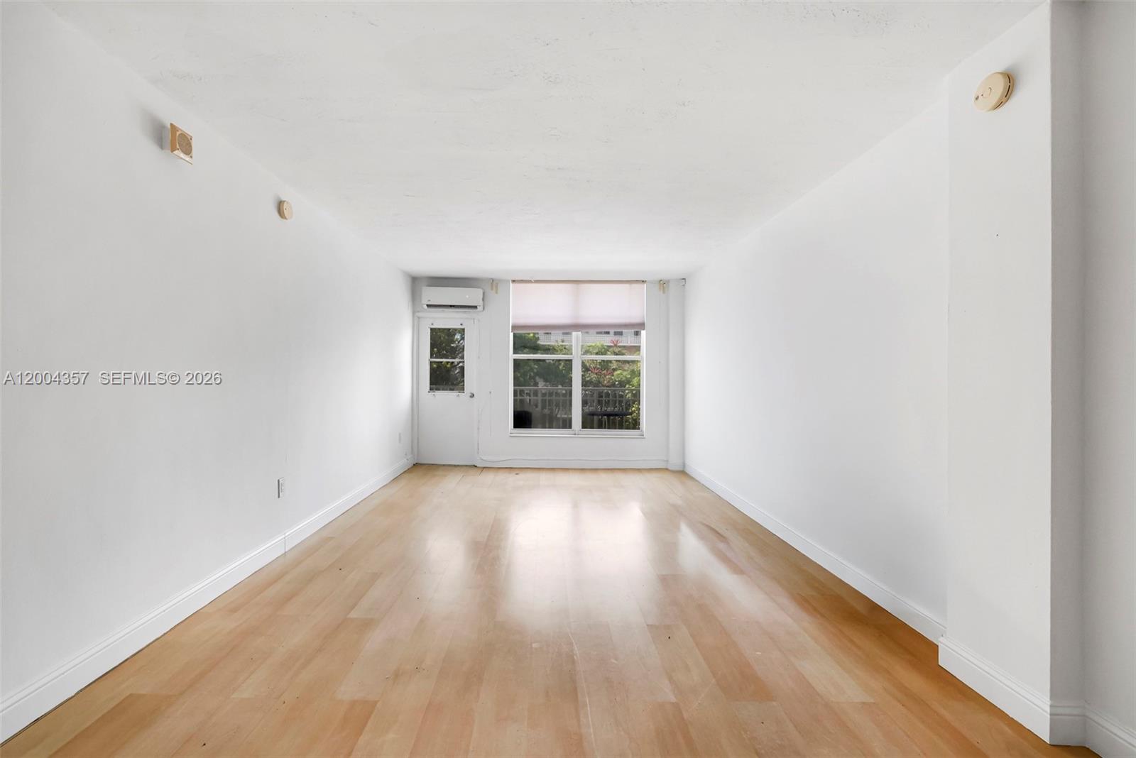 An empty room features white walls, light wood flooring, a window, and a balcony door — 1300 Lincoln Rd # B402, Miami Beach FL 33139, MIAMI BEACH, FL