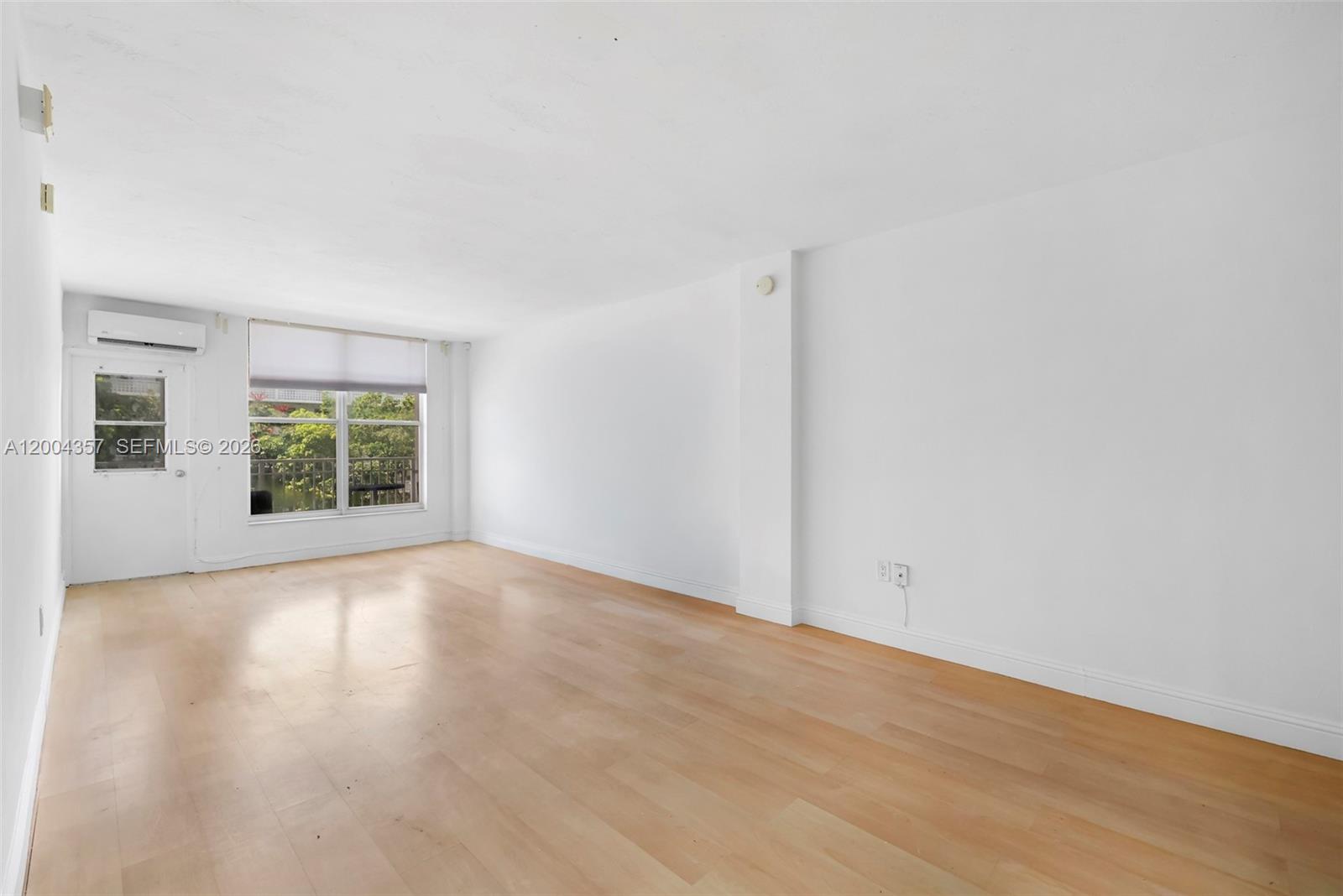 An empty room features white walls, light wood flooring, a window, and a glass door — 1300 Lincoln Rd # B402, Miami Beach FL 33139, MIAMI BEACH, FL