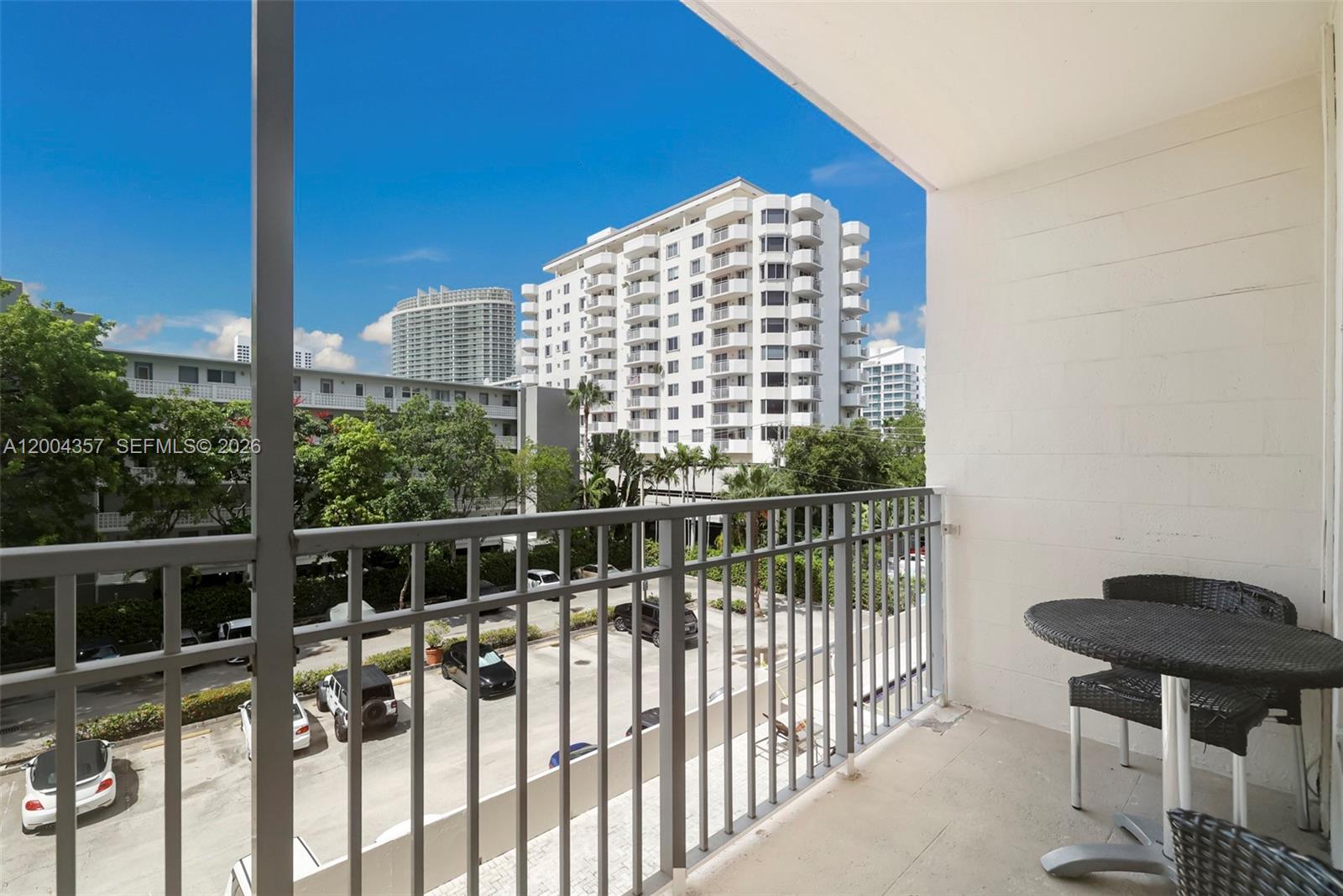 A balcony features a metal railing, a small table with chairs, and a view of a parking lot and buildings — 1300 Lincoln Rd # B402, Miami Beach FL 33139, MIAMI BEACH, FL