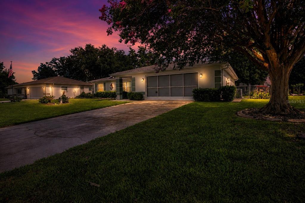 A single-story house with a concrete driveway and a large tree at twilight — 6169 SW 100TH LOOP, OCALA, FL