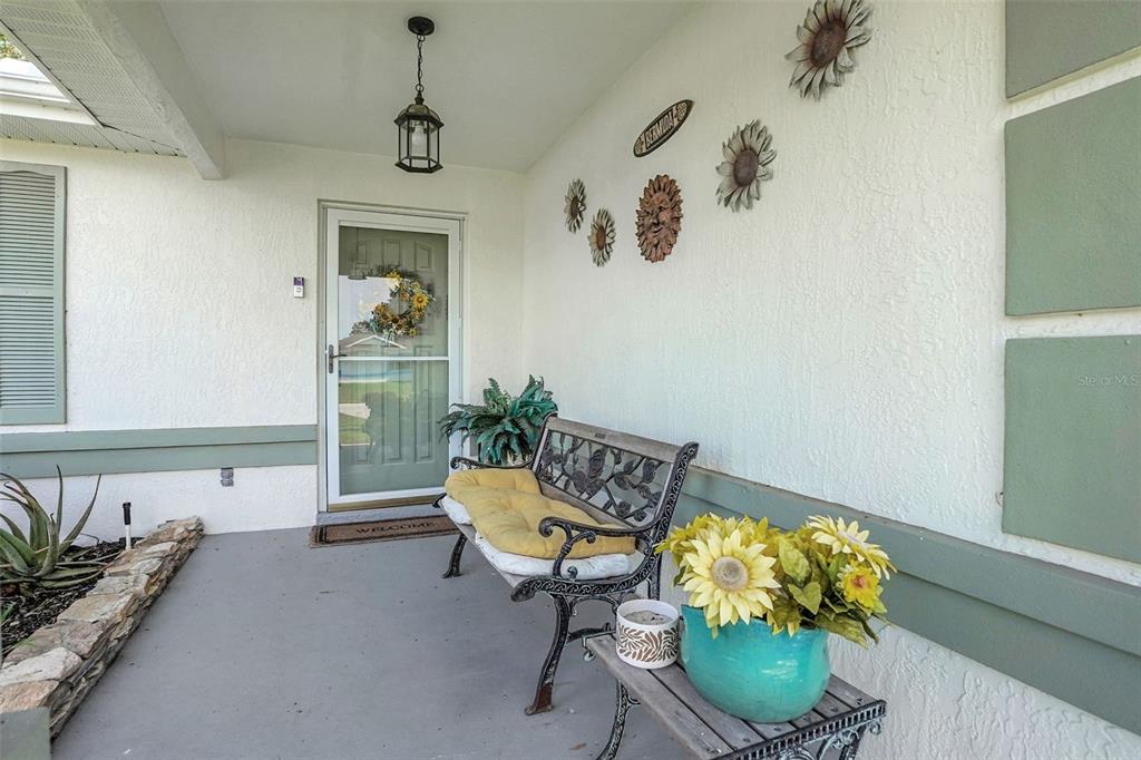 A covered front porch features a metal bench, a potted plant, and wall-mounted floral decorations — 6169 SW 100TH LOOP, OCALA, FL