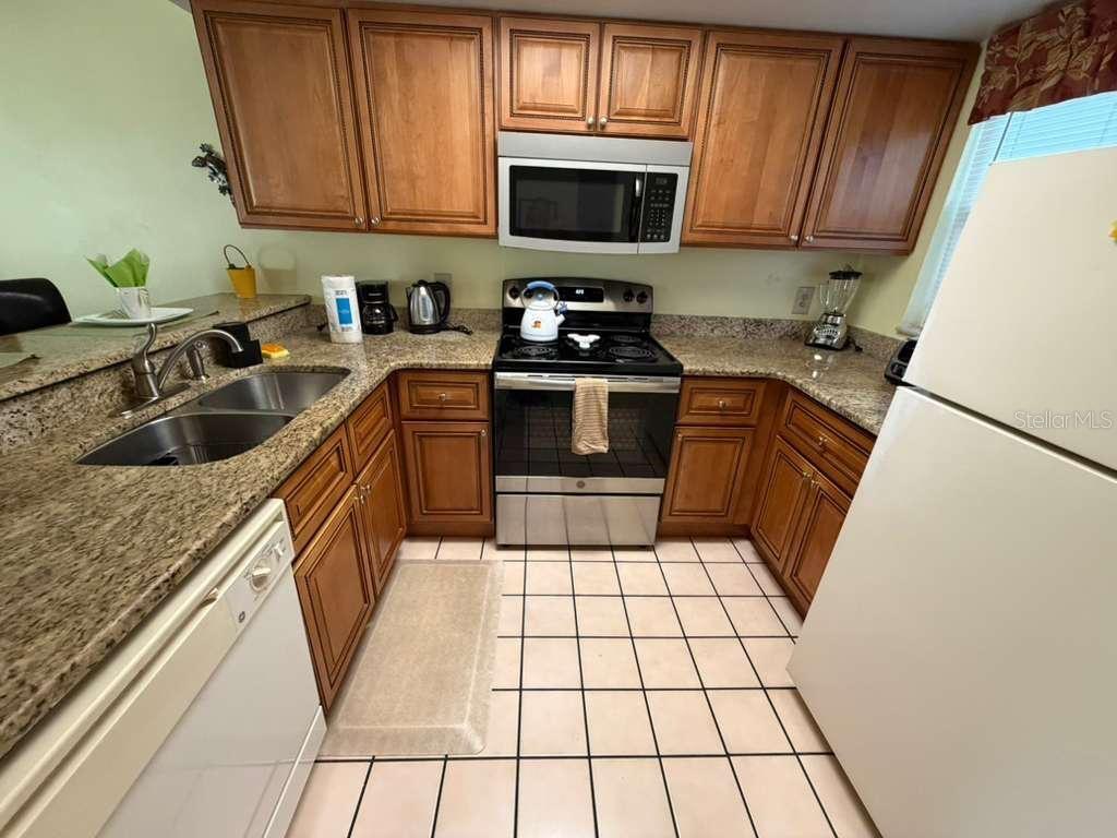 A kitchen features wood cabinets, granite countertops, stainless steel appliances, and white tile flooring — 3197 SEA WORLD COURT, KISSIMMEE, FL