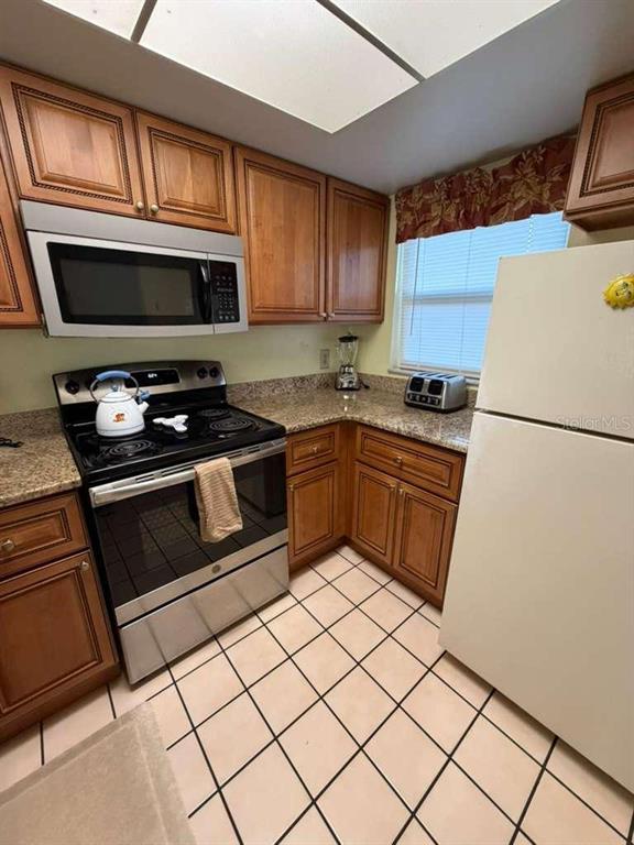 A kitchen features wood cabinets, stainless steel appliances, granite countertops, and light-colored tiled flooring — 3197 SEA WORLD COURT, KISSIMMEE, FL
