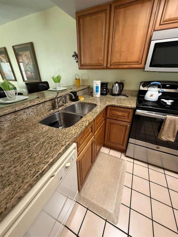 A kitchen features wood cabinets, granite countertops, a stainless steel stove, and tiled flooring — 3197 SEA WORLD COURT, KISSIMMEE, FL