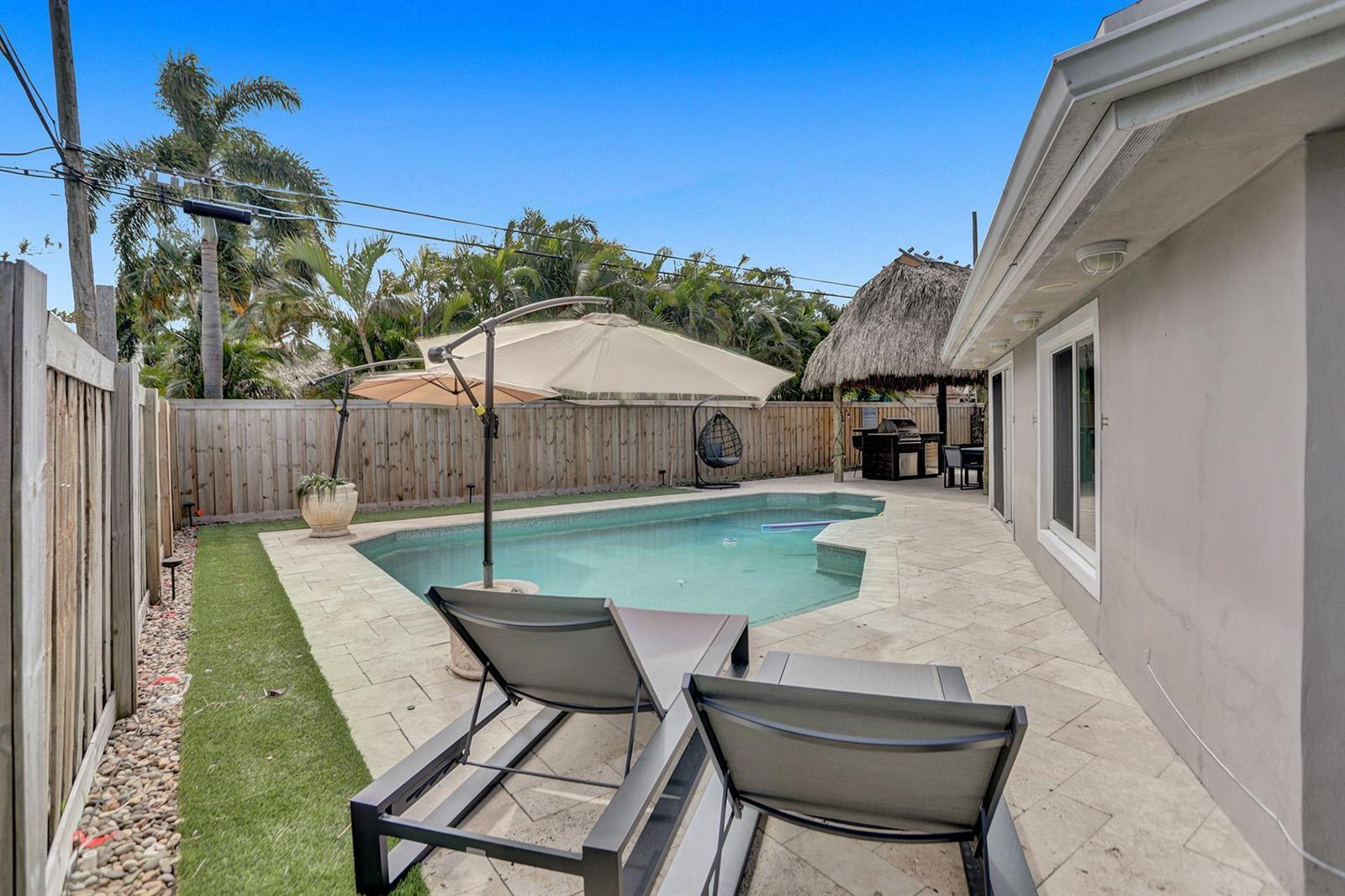 A backyard features a swimming pool, lounge chairs, a patio, and a tiki hut — 470 SE 4th Court, Pompano Beach FL 33060, POMPANO BEACH, FL