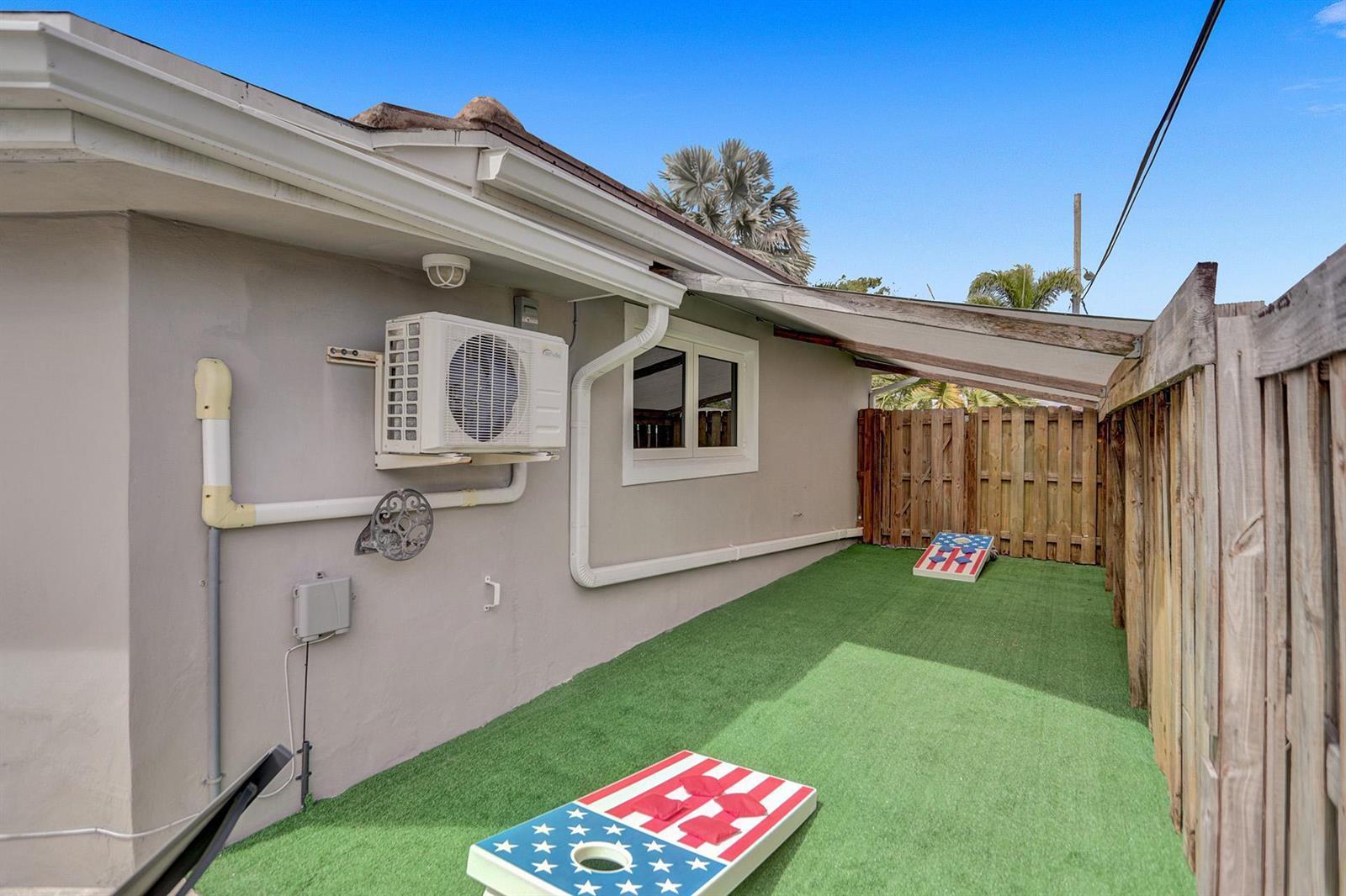 A side yard with artificial turf, a wooden fence, and two American flag cornhole boards — 470 SE 4th Court, Pompano Beach FL 33060, POMPANO BEACH, FL