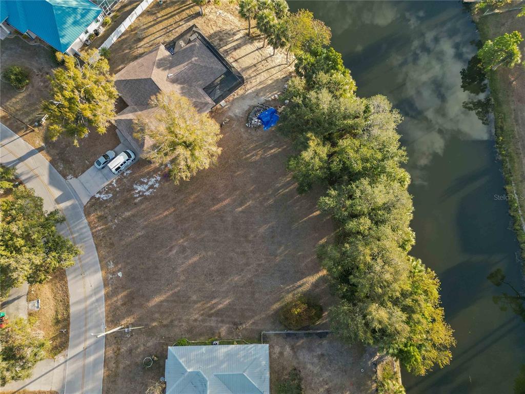 An aerial view shows a vacant residential lot situated between a house and a canal — 20551 ALBURY DRIVE, PORT CHARLOTTE, FL