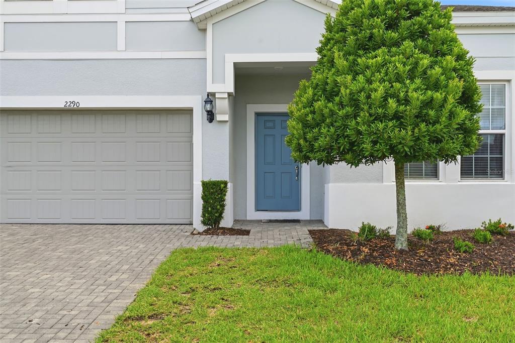 A light gray house exterior features a blue front door, a garage, and a tree — 2290 LELANI CIRCLE, DAVENPORT, FL