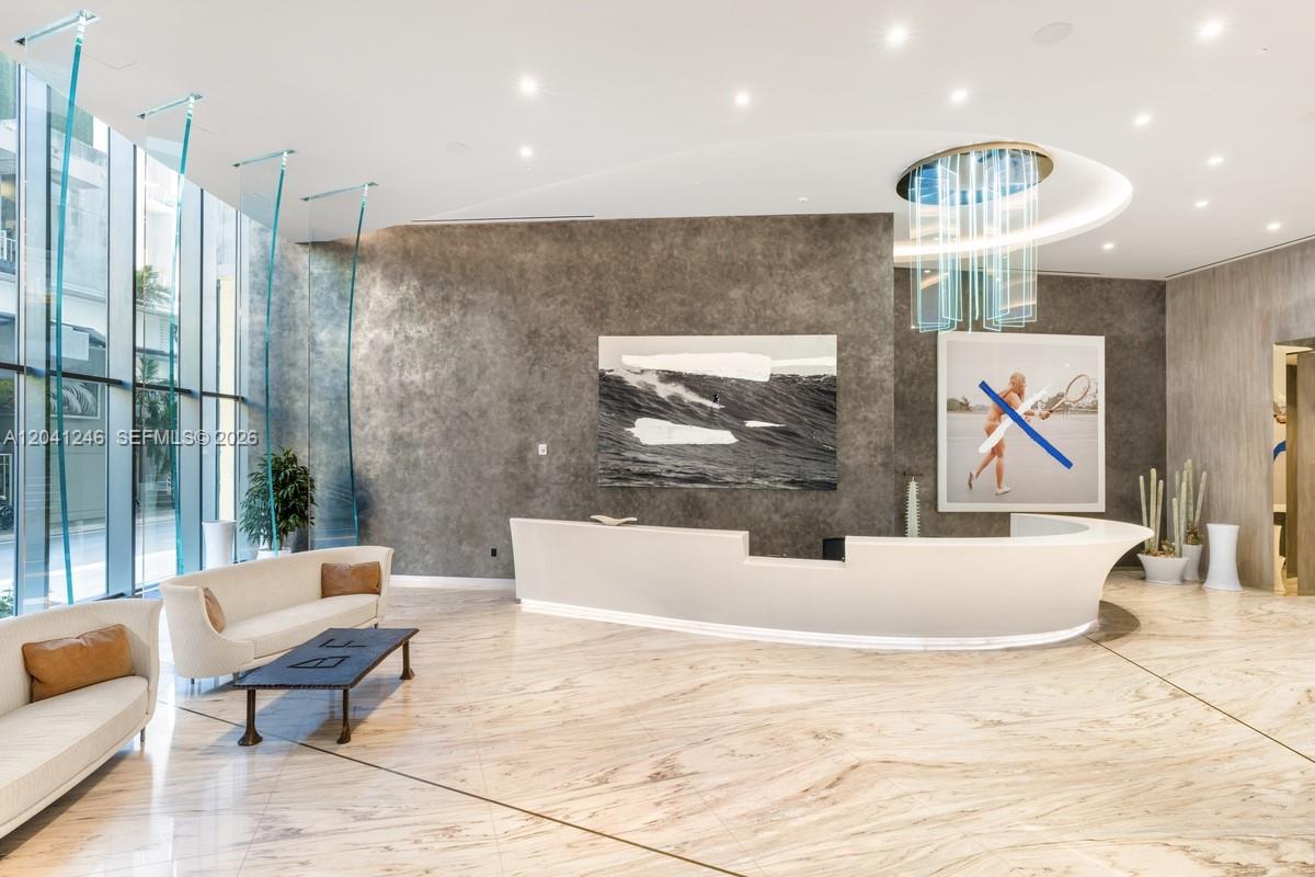 A modern lobby features a curved white reception desk, marble flooring, and two large wall artworks — 1000 Brickell Plz # 2101, Miami FL 33131, MIAMI, FL