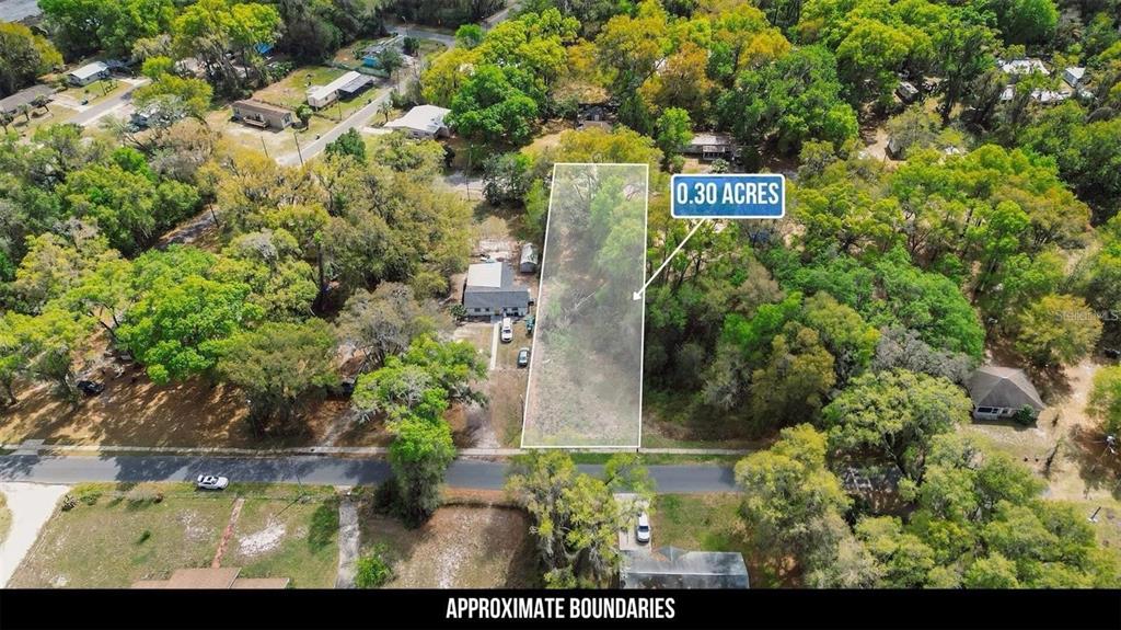 An aerial view shows a rectangular, wooded vacant lot outlined in white among residential properties — LAWRENCE ST, WILDWOOD, FL