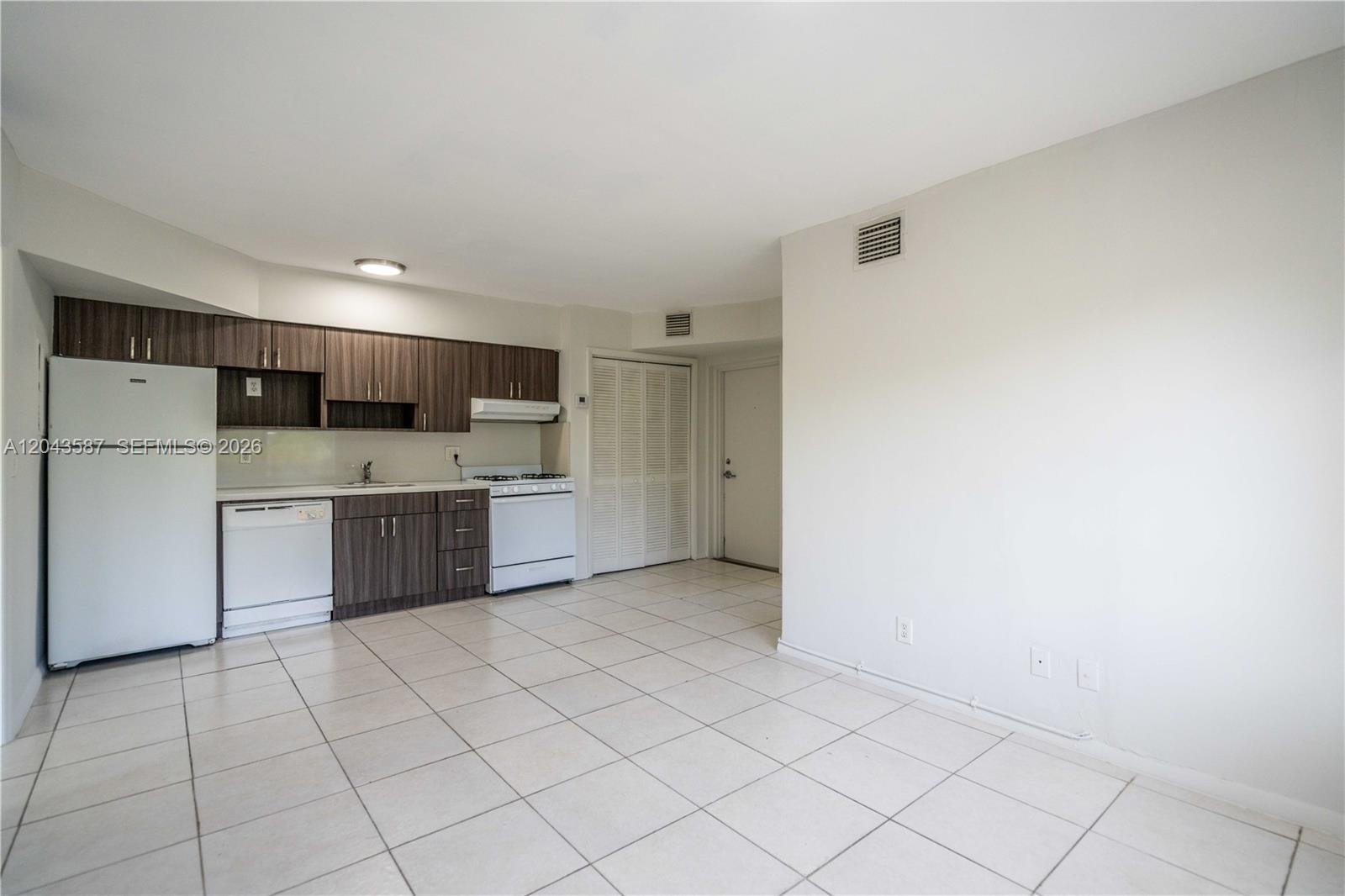 A kitchen with dark wood cabinets and white appliances opens into a tiled living area — 666 NE 80th St # 6, Miami FL 33138, MIAMI, FL