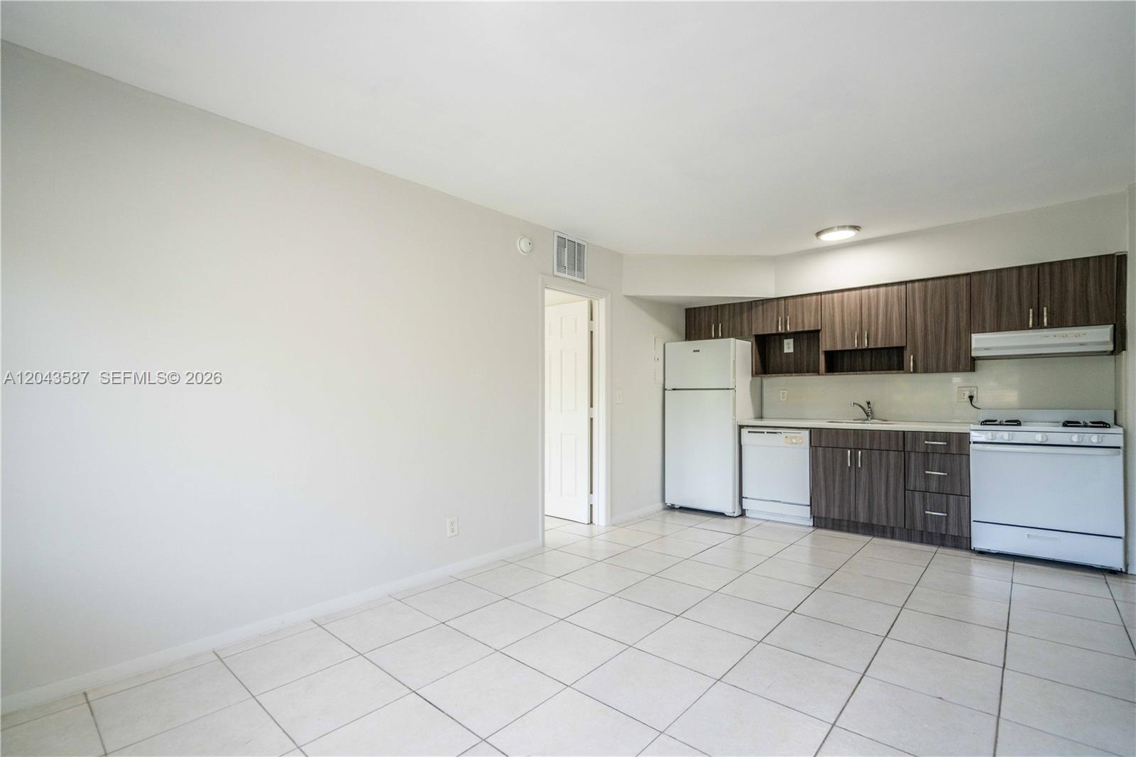 A kitchen features dark wood cabinets, white appliances, and light-colored tile flooring — 666 NE 80th St # 6, Miami FL 33138, MIAMI, FL