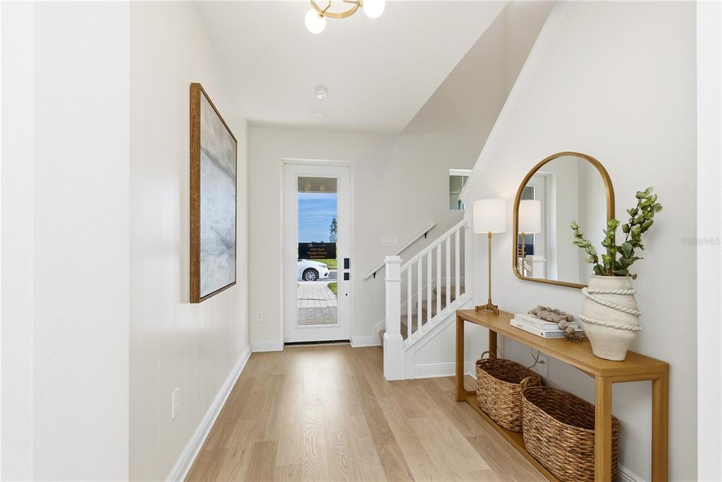 A bright entryway features light wood flooring, a white staircase, and a console table — 17818 BROADLEAF LOOP, VENICE, FL