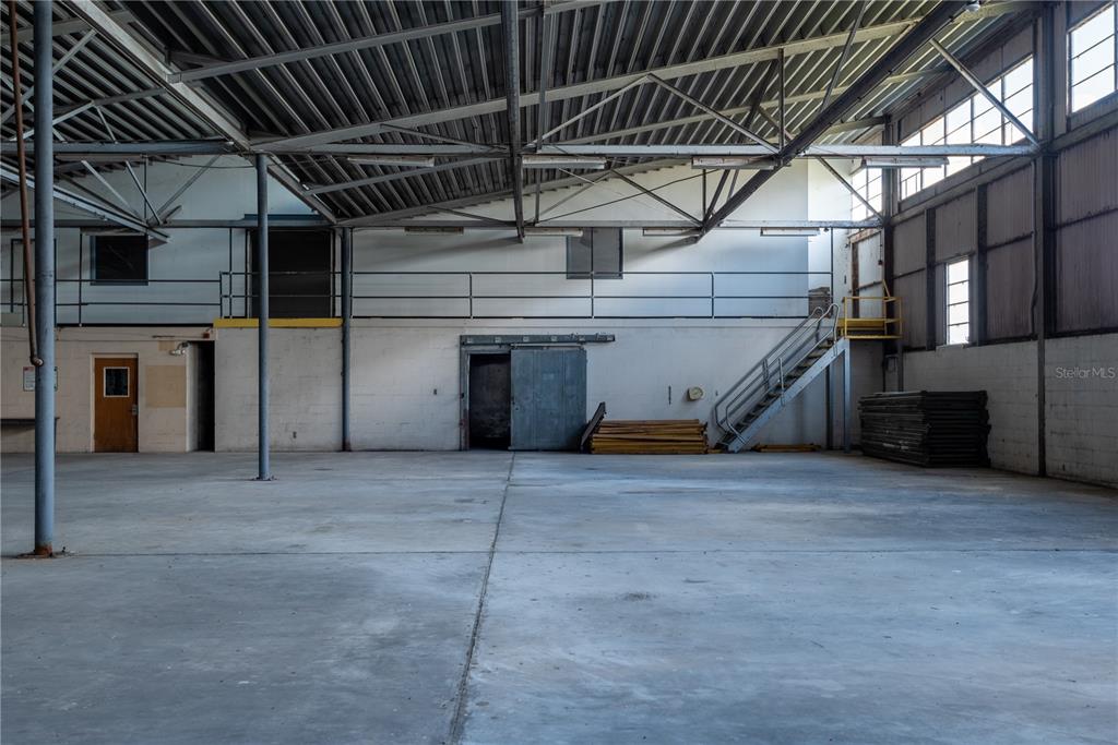 A large, empty industrial warehouse space features concrete floors, exposed metal trusses, and a staircase — 5000 SE HWY 31 UNIT W, ARCADIA, FL
