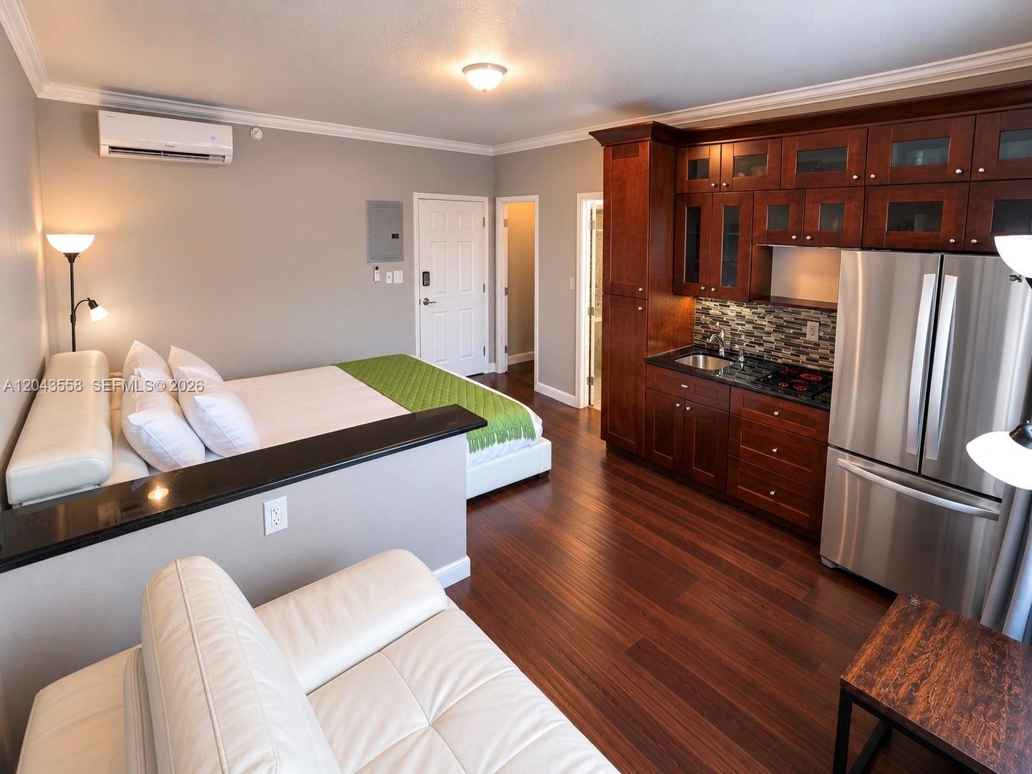 A studio apartment features a kitchenette with dark wood cabinets, stainless appliances, and a bed — 3025 Indian Creek Dr # 320, Miami Beach FL 33140, MIAMI BEACH, FL