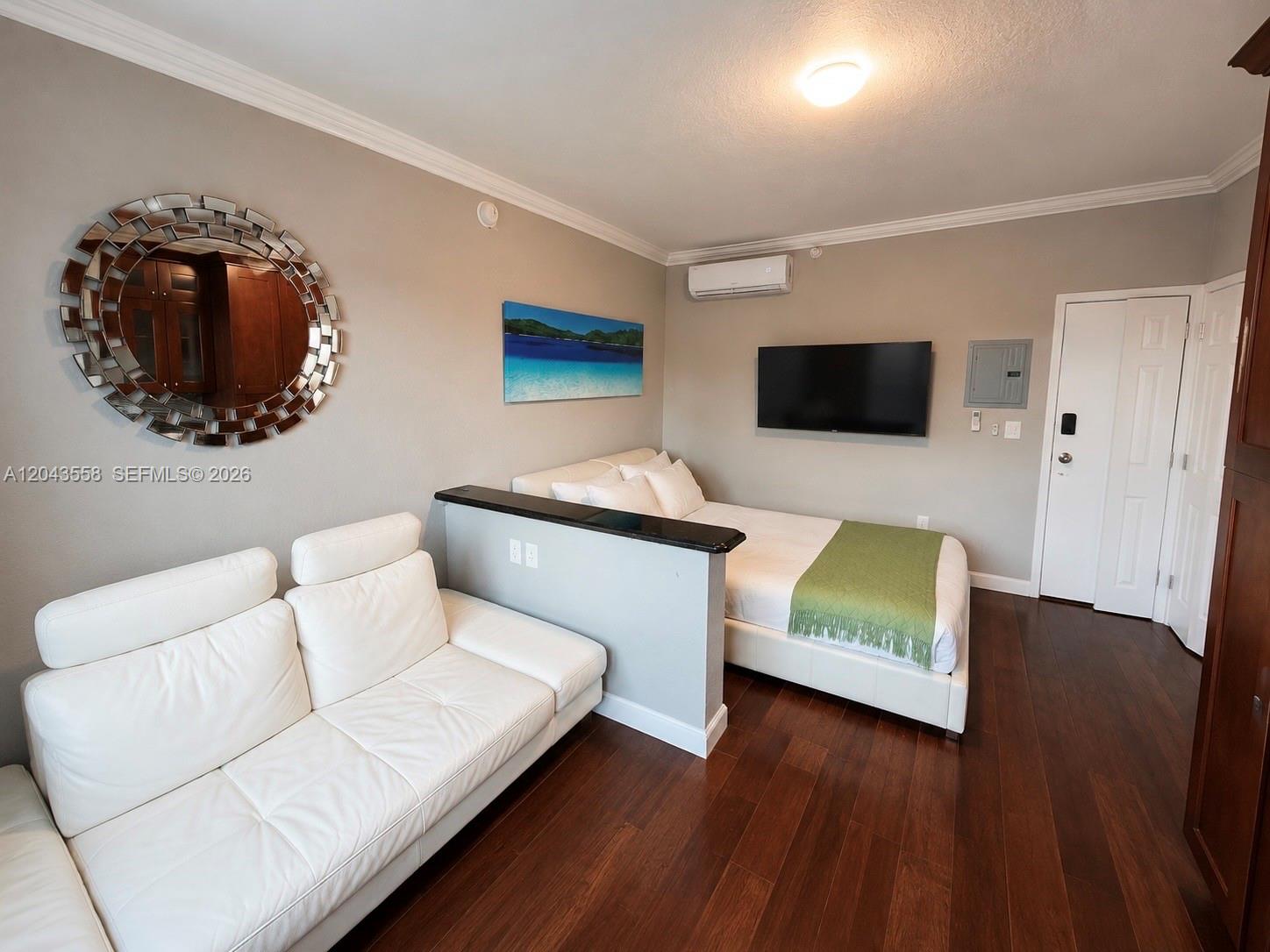 A studio apartment features a white sofa, a bed behind a partition, and dark flooring — 3025 Indian Creek Dr # 320, Miami Beach FL 33140, MIAMI BEACH, FL