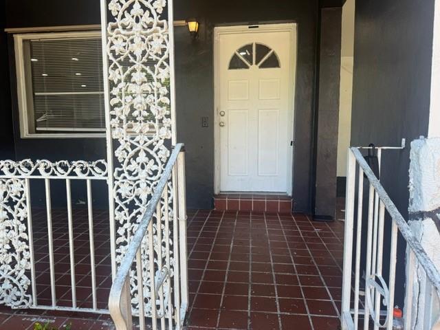 A white front door with a decorative metal railing stands on a tiled porch — 740 NW 42nd St, Miami FL 33127, MIAMI, FL