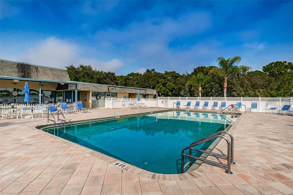 A rectangular swimming pool with a metal ladder sits on a paved patio area — 39820 US HIGHWAY 19 N UNIT 153, TARPON SPRINGS, FL