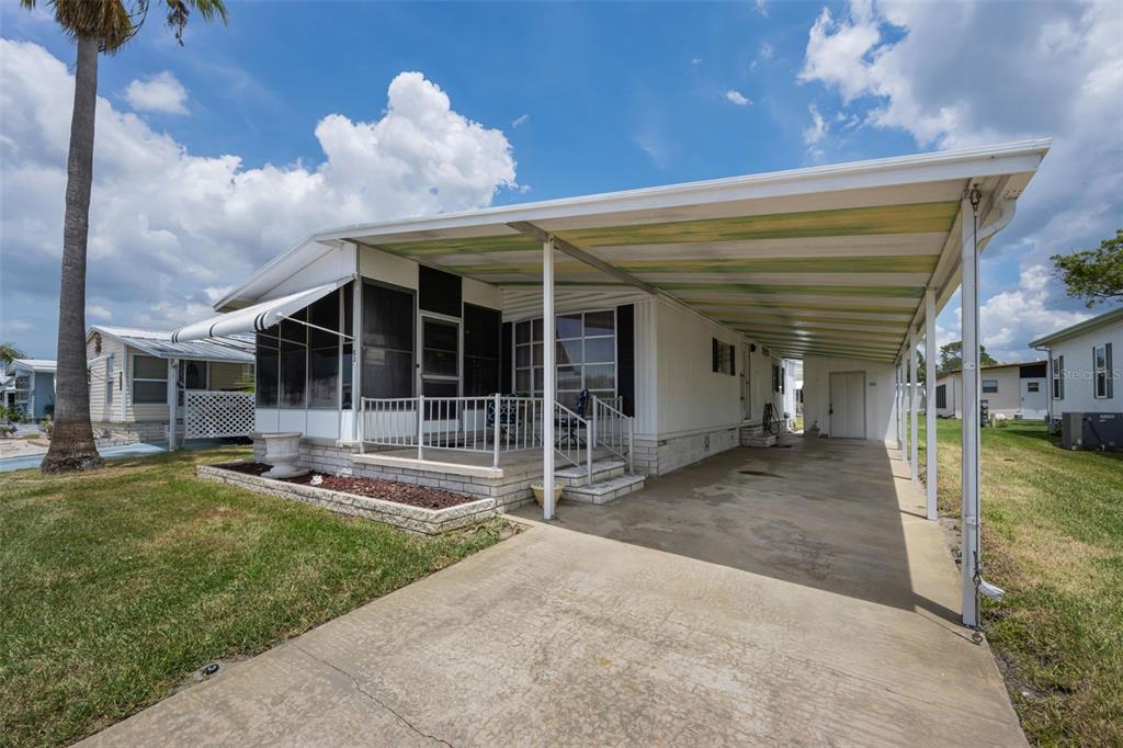 A mobile home features a screened-in porch, a concrete driveway, and an attached carport — 39820 US HIGHWAY 19 N UNIT 153, TARPON SPRINGS, FL