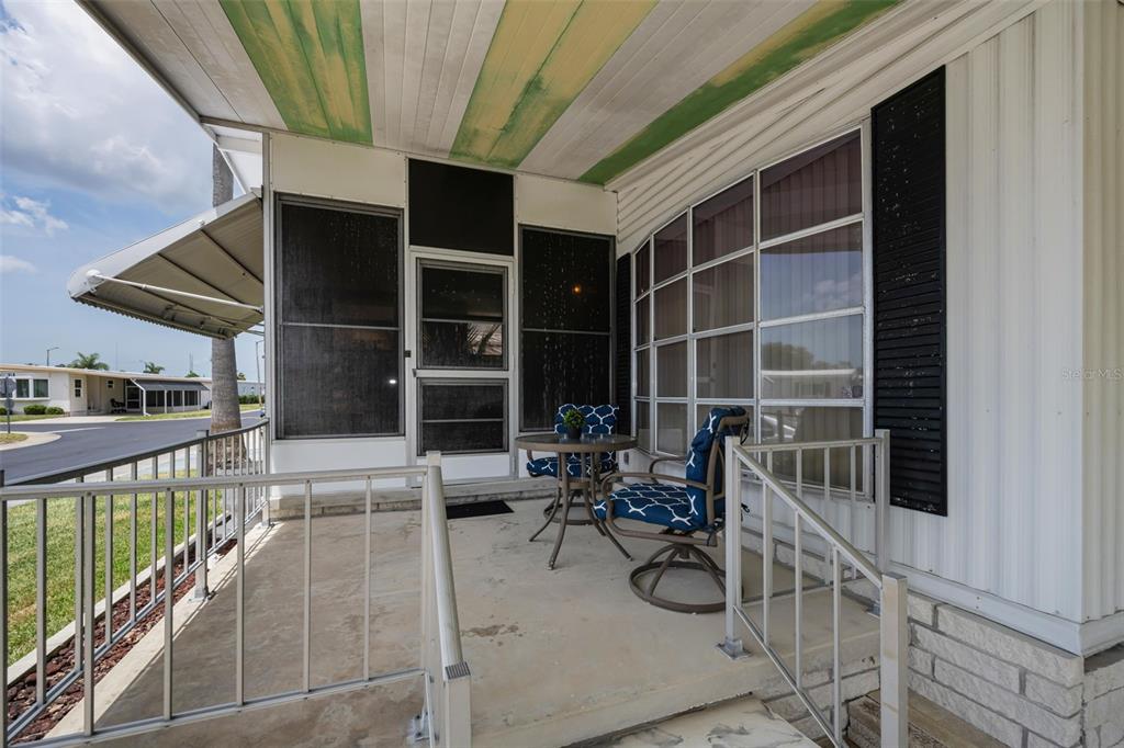 A covered concrete porch features a small bistro set and a screened-in entry door — 39820 US HIGHWAY 19 N UNIT 153, TARPON SPRINGS, FL