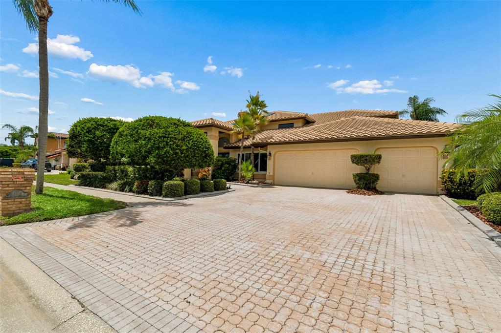 A tan house with a tiled roof and a large paved driveway under a blue sky — 9815 BAY ISLAND DRIVE, TAMPA, FL